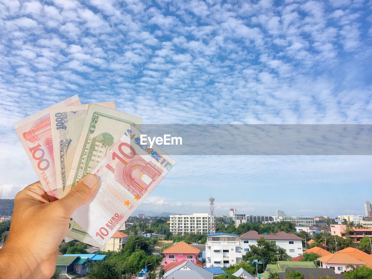 Midsection of person holding banknotes against sky