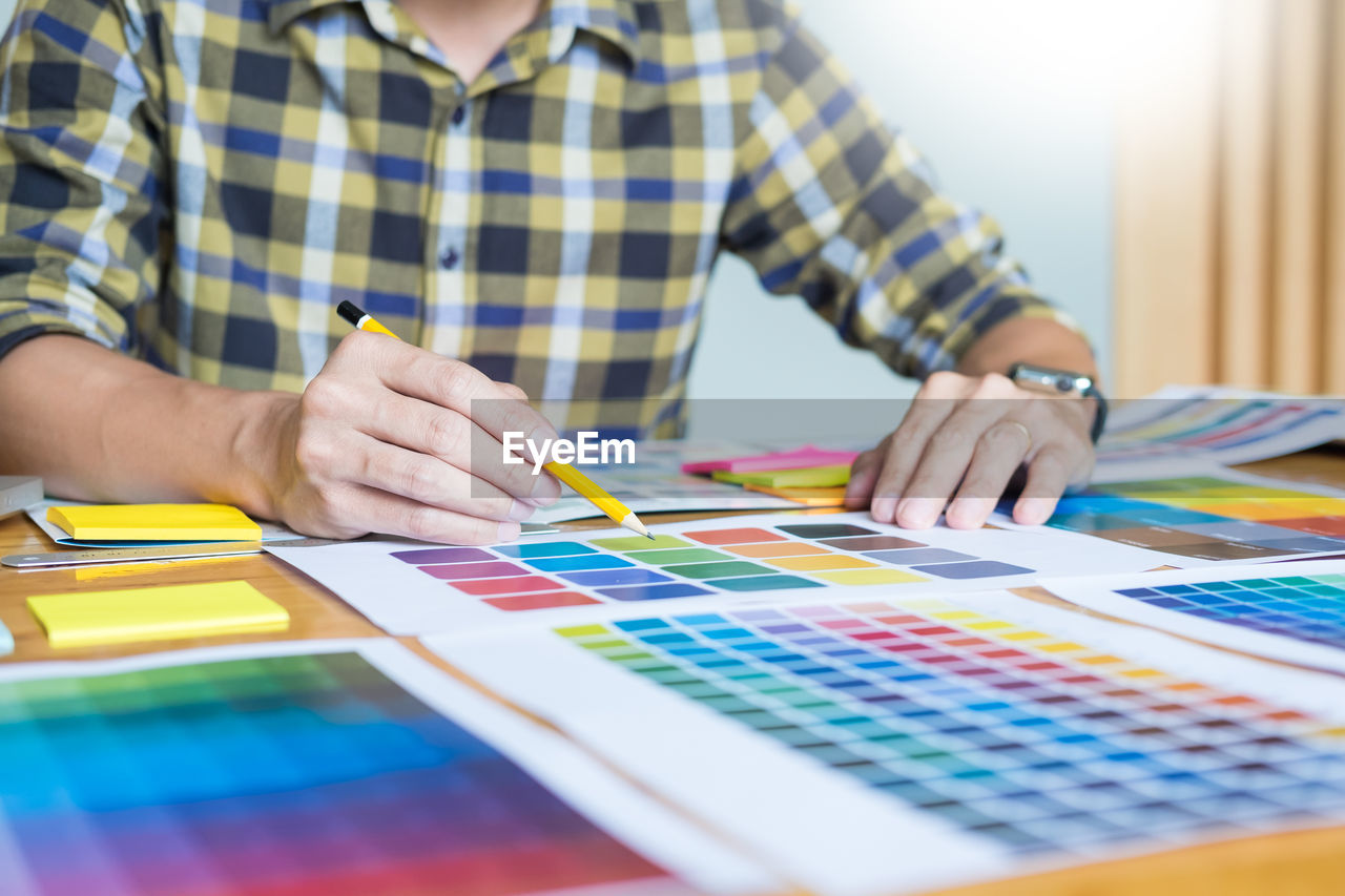 Midsection of man drawing on color swatches at office