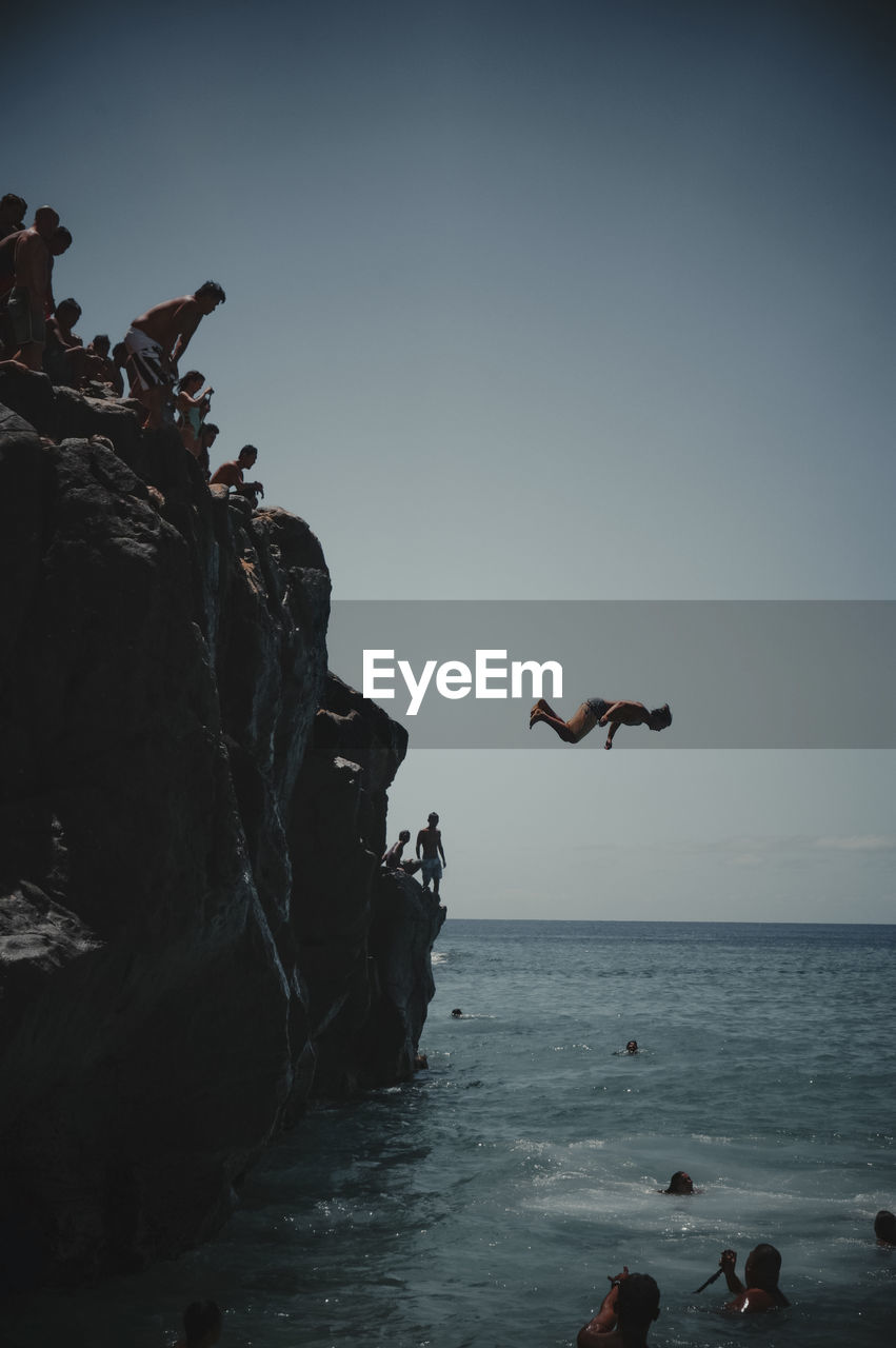 GROUP OF PEOPLE ON ROCKS BY SEA