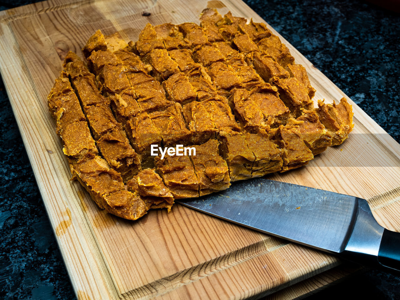 Home made dog treats made of pumpkin on a wooden cutting block with a knife.