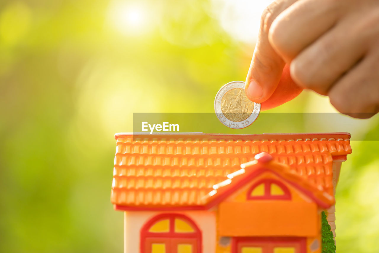 Close-up of hand holding coin over toy house