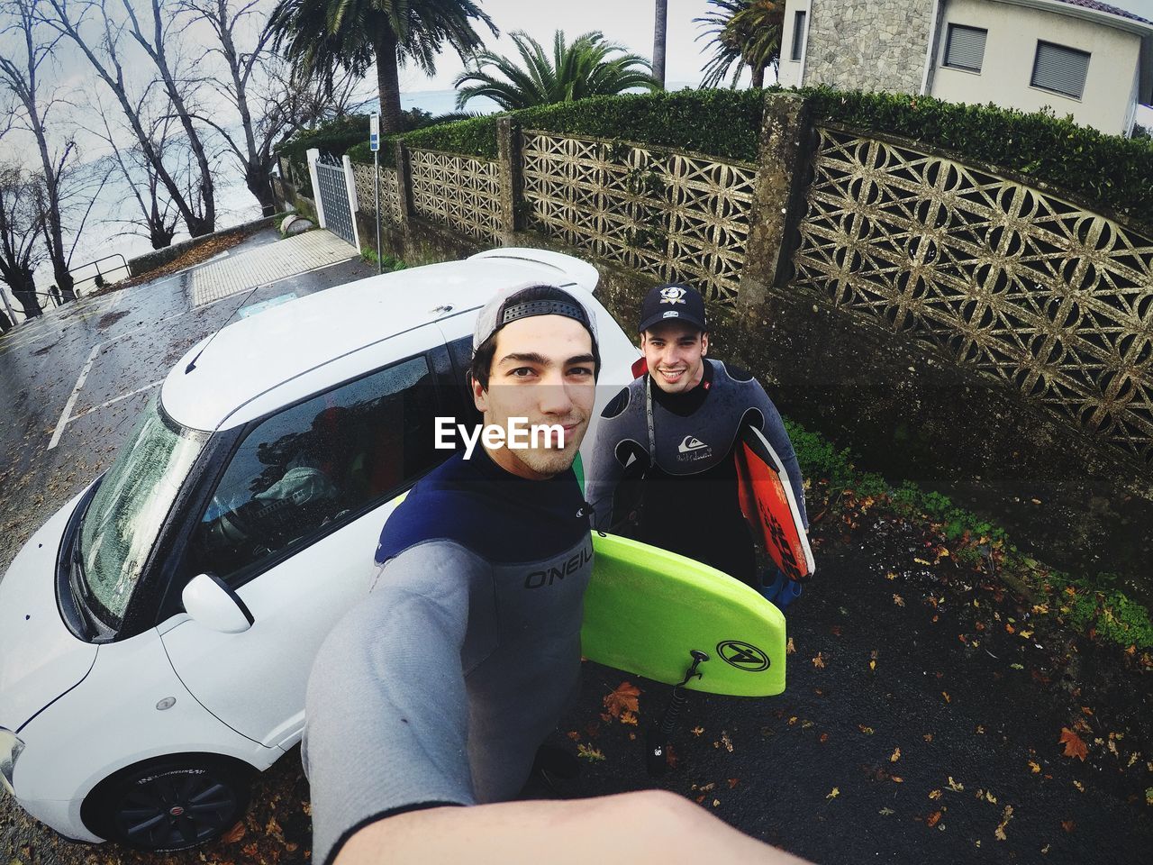 High angle portrait of smiling friends with surfboards standing by car on street