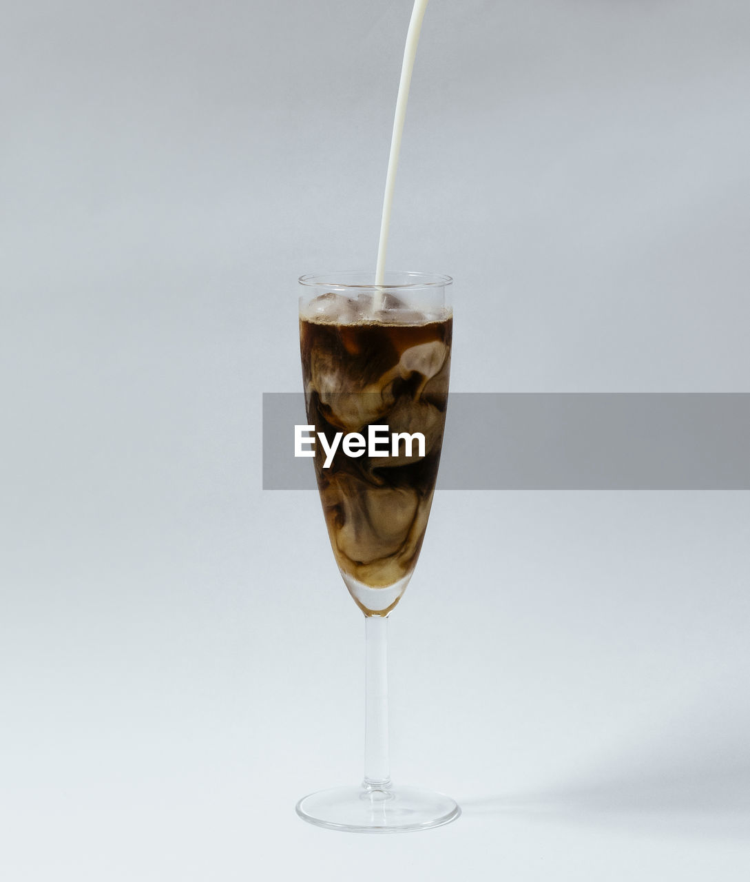 Milk pouring into iced coffee swirling on white background