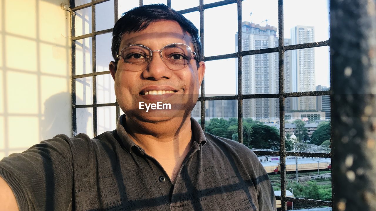 PORTRAIT OF SMILING YOUNG MAN WEARING EYEGLASSES