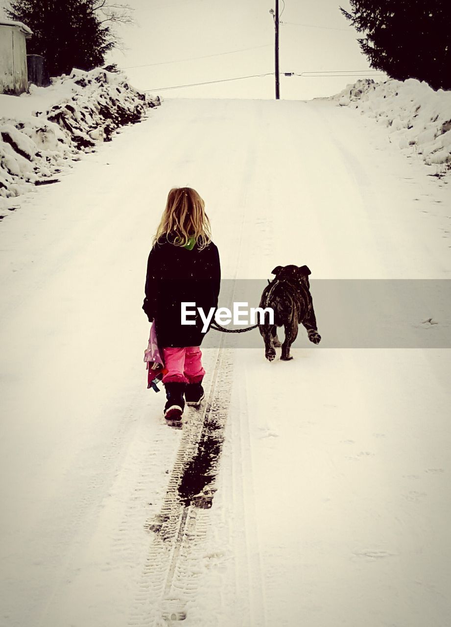 Rear view of girl with dog walking on snow covered street