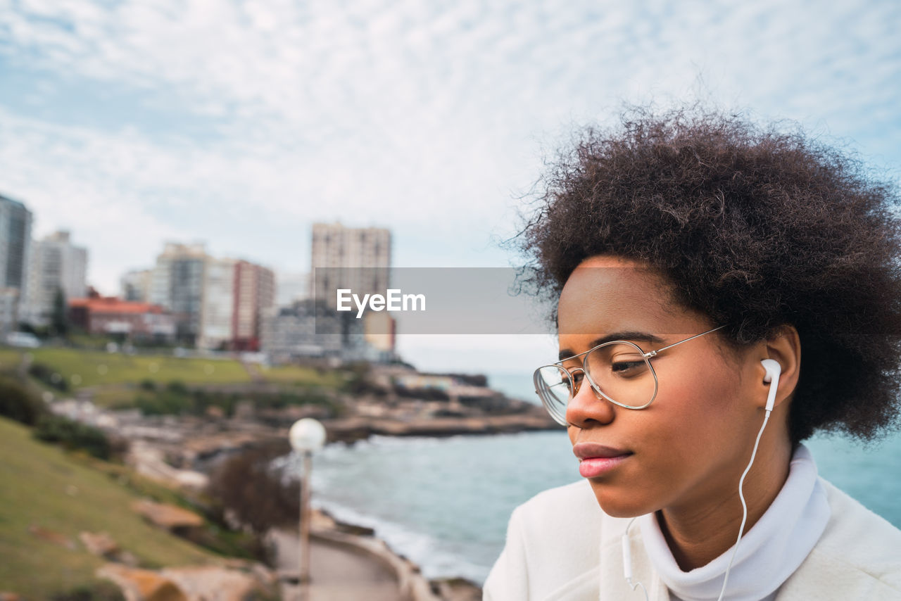 Portrait of beautiful young woman in city against sky