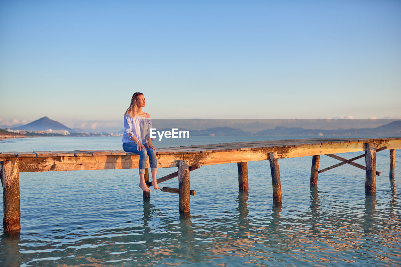 Woman sitting on pier in sea against clear sky