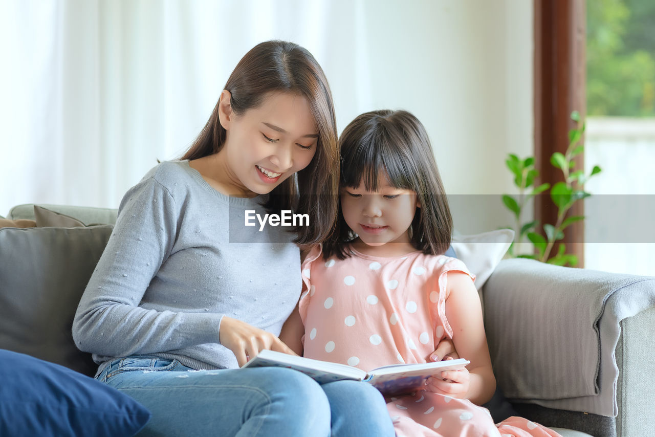Happy asian mother teaching her cute kid daughter to studying in living room at home