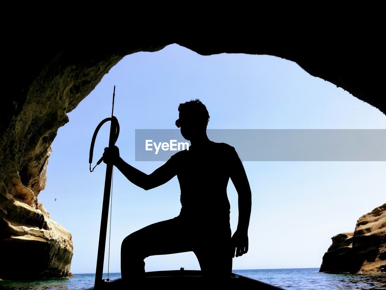 SILHOUETTE MAN STANDING ON ROCK AT SEA SHORE AGAINST CLEAR SKY