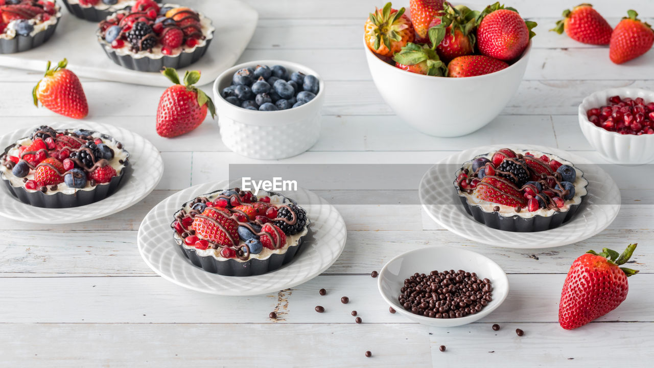 Sweet mixed berry cheesecake tarts with bowls of extra berries.