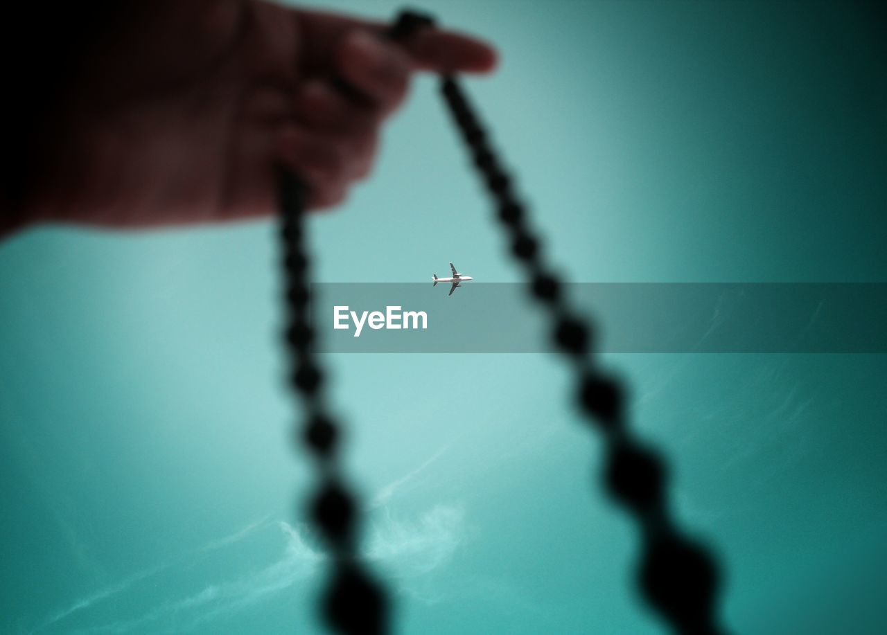 Airplane seen through bead necklace held by man