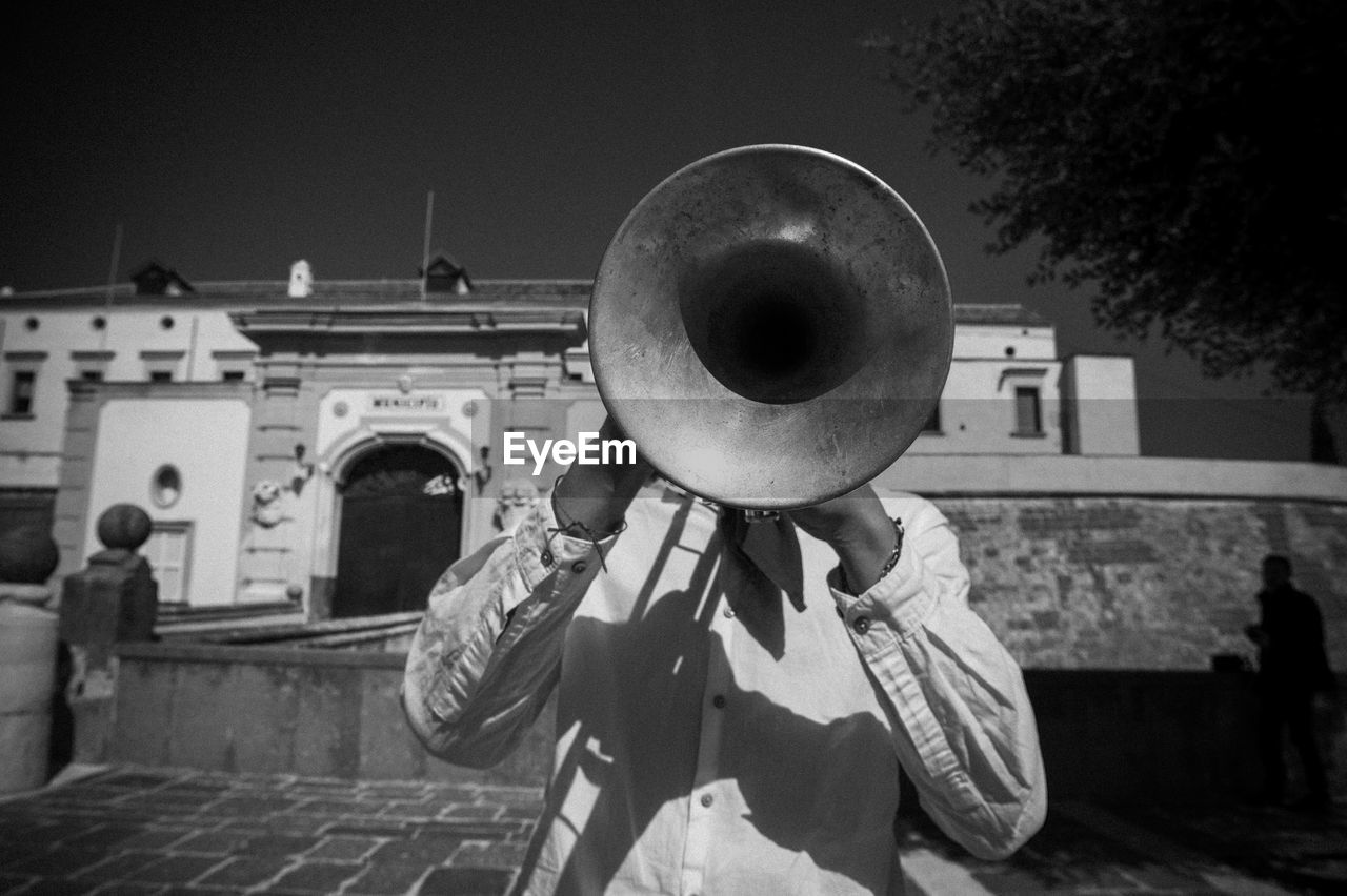 Musician playing trumpet while standing against building