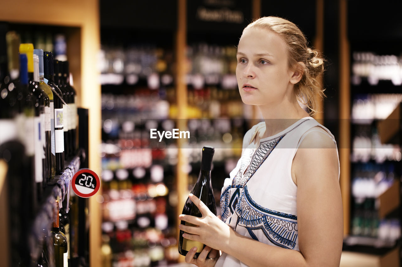 Young woman buying liquor in supermarket