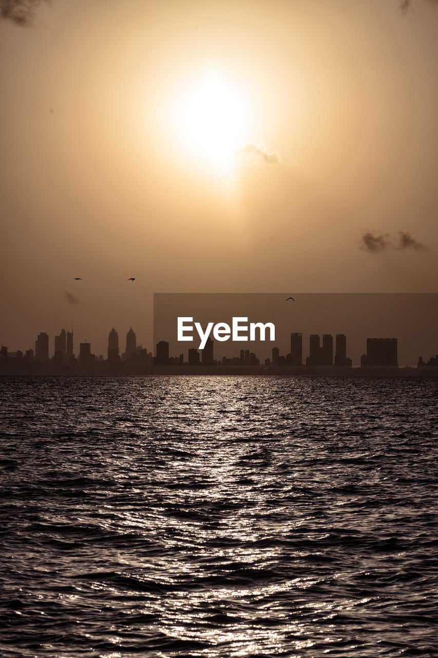 SCENIC VIEW OF SEA BY BUILDINGS AGAINST SKY DURING SUNSET