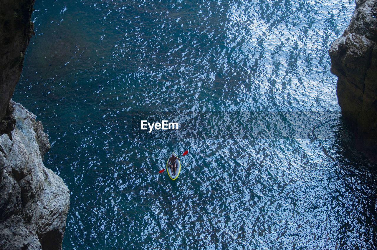 HIGH ANGLE VIEW OF PEOPLE ON ROCK AT SEA