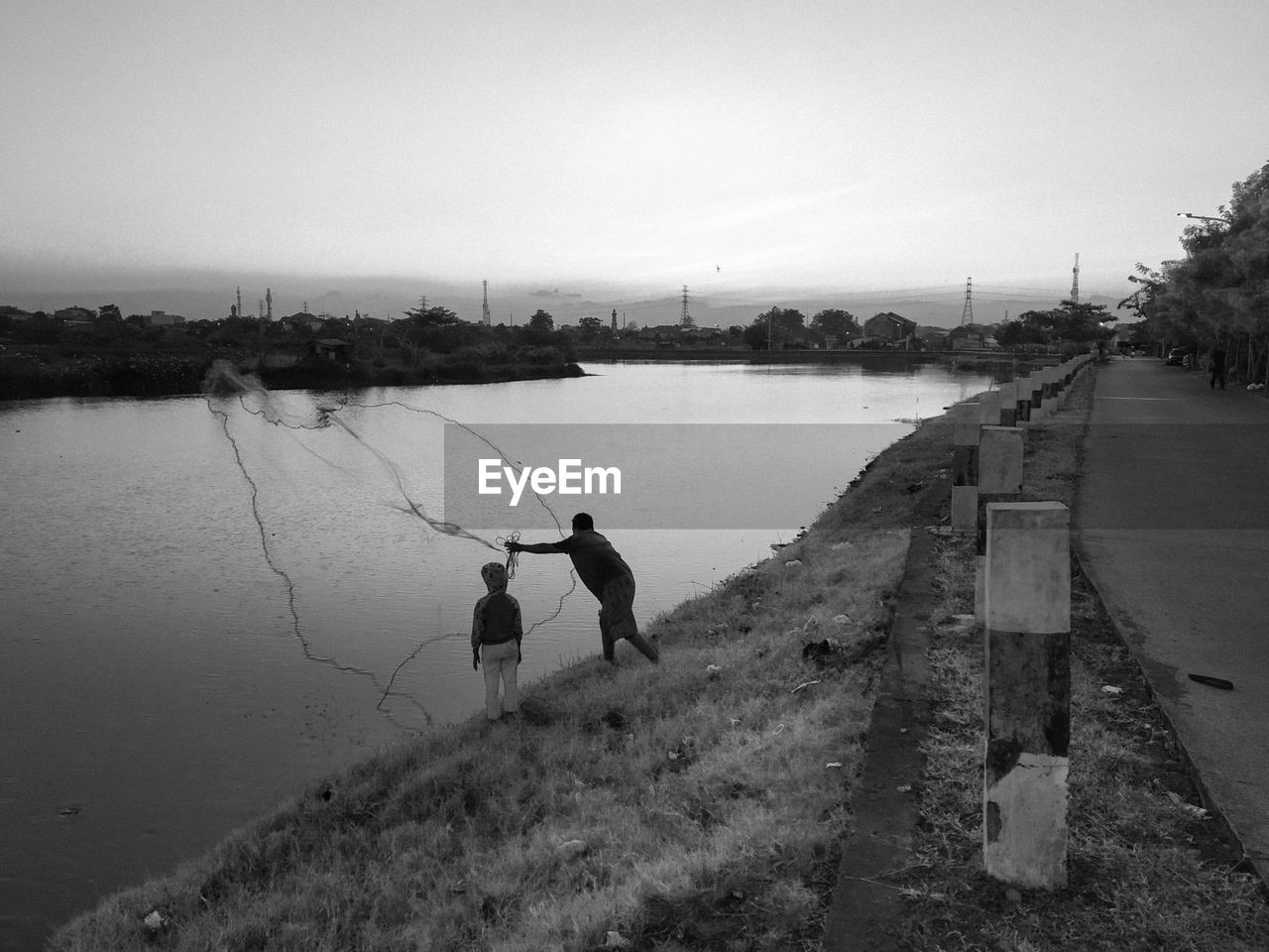 MEN FISHING AT LAKE AGAINST SKY