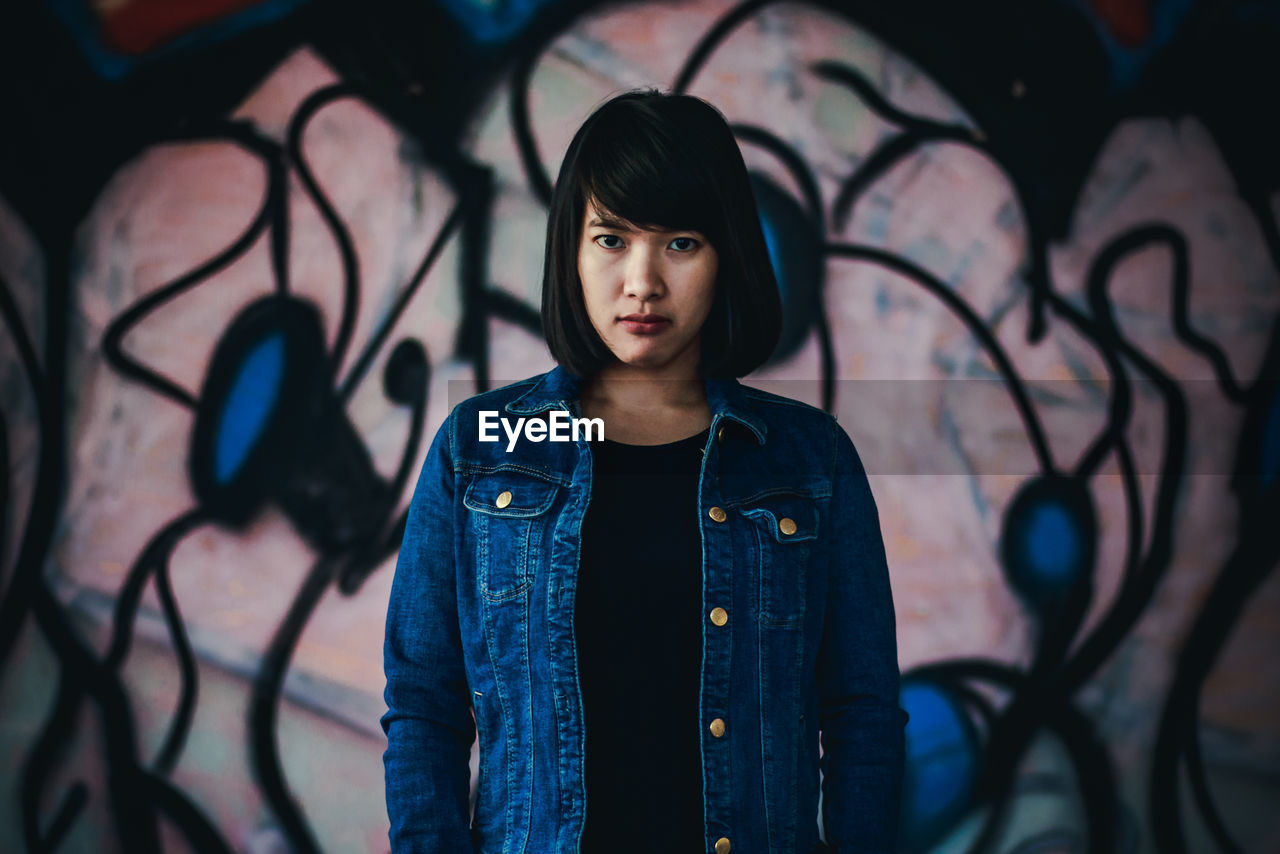 Portrait of woman standing by graffiti wall