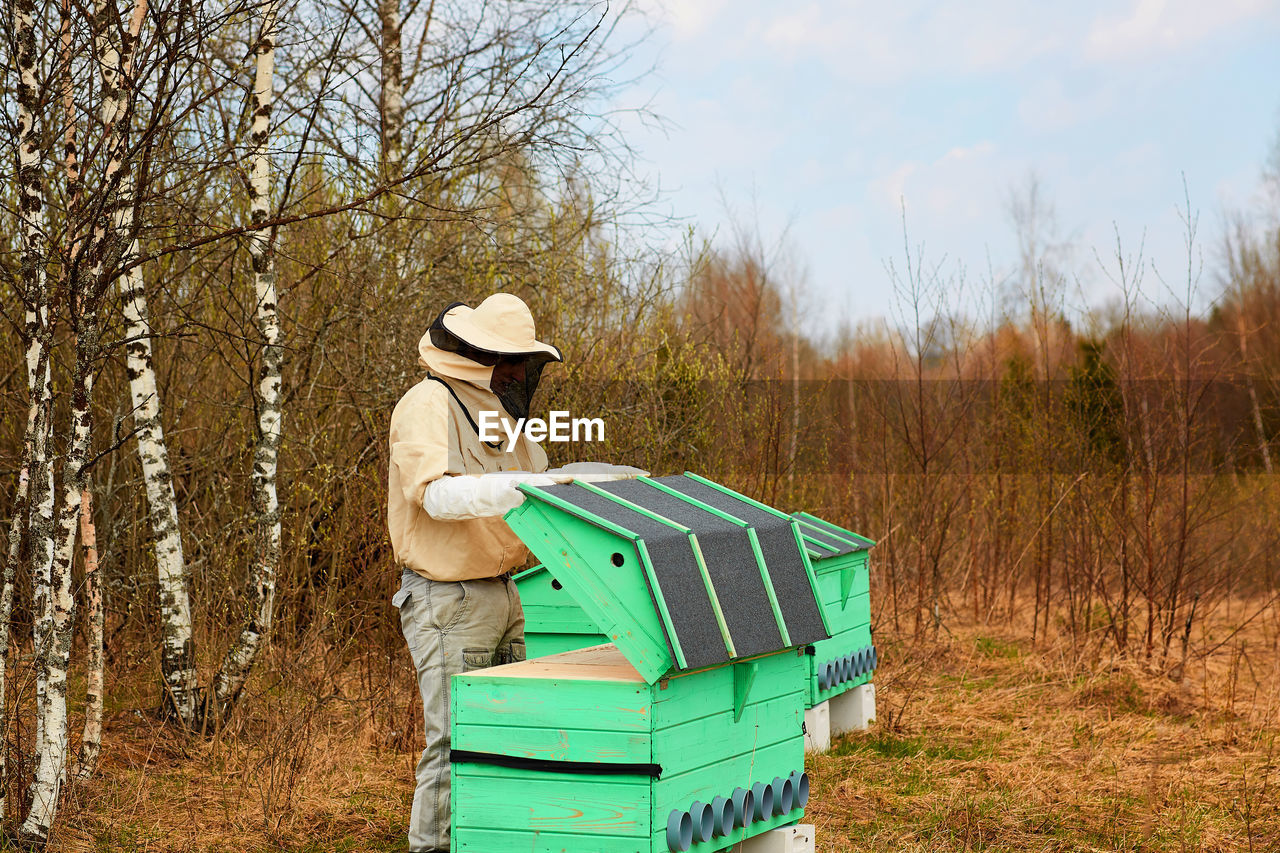 Man repairing wooden boxes against bare trees