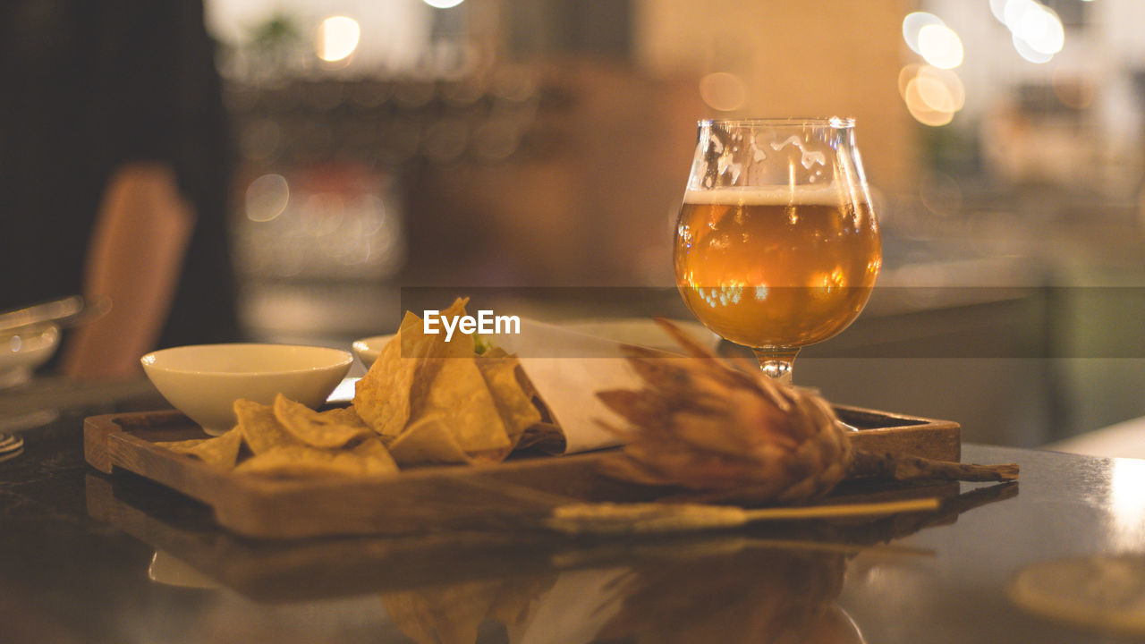Close-up of beer glass with flower and nacho served on table