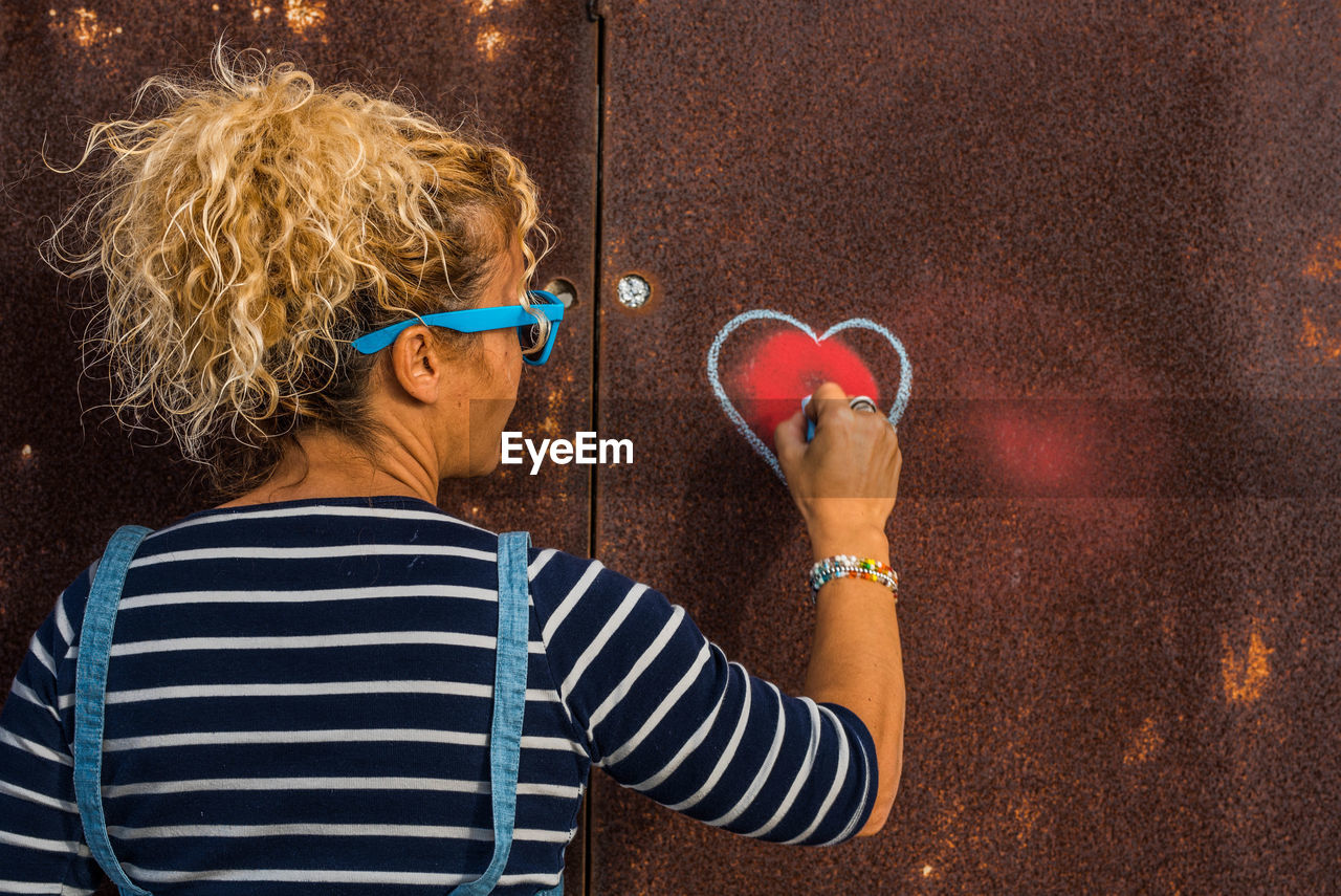 Rear view of woman making heart shape on rusty metal