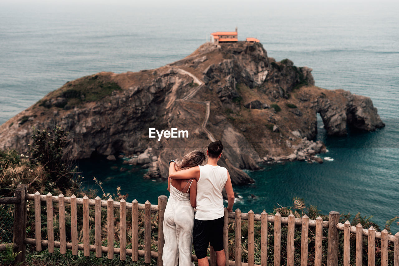 Rear view of couple standing by railing over sea