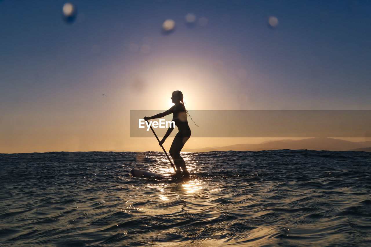 Female sup surfer at sunset time