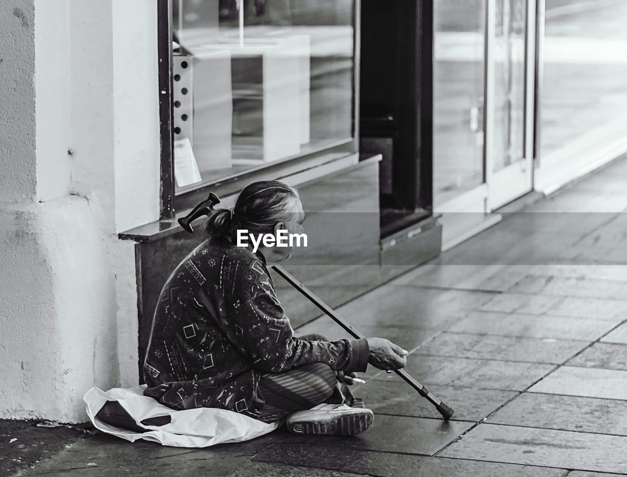 Woman sitting on footpath by window