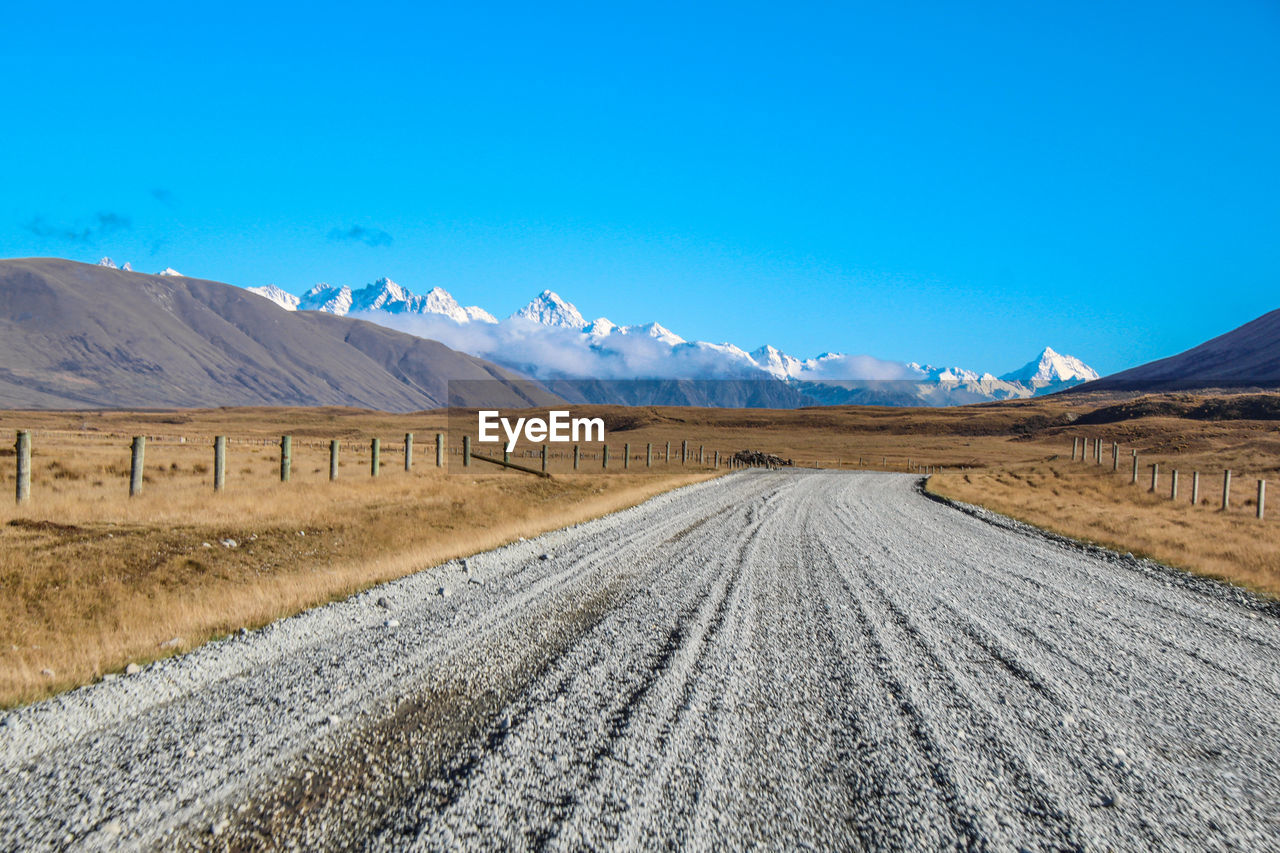 Scenic view of empty road by mountains against blue sky