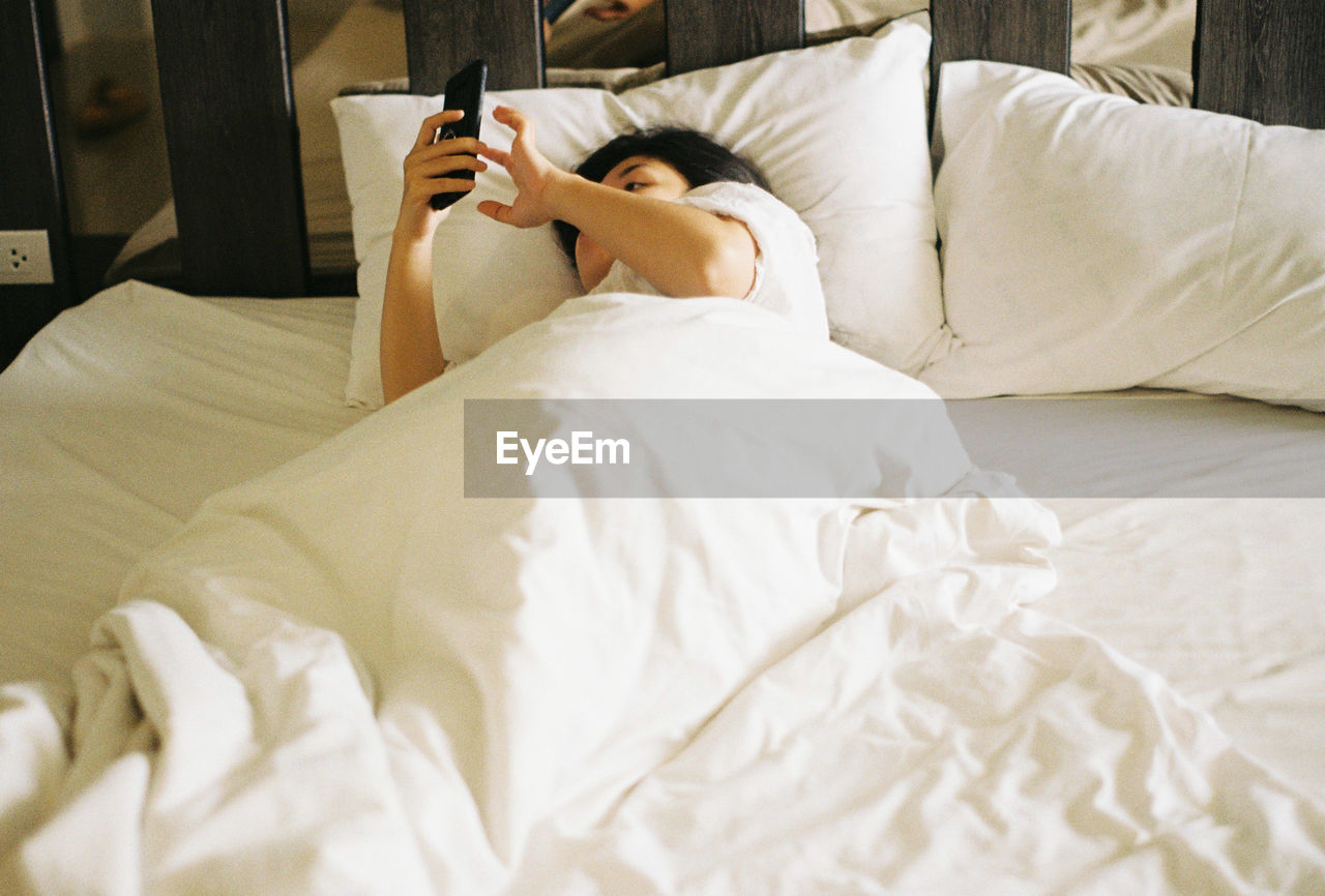 High angle view of woman using phone while lying on bed at home