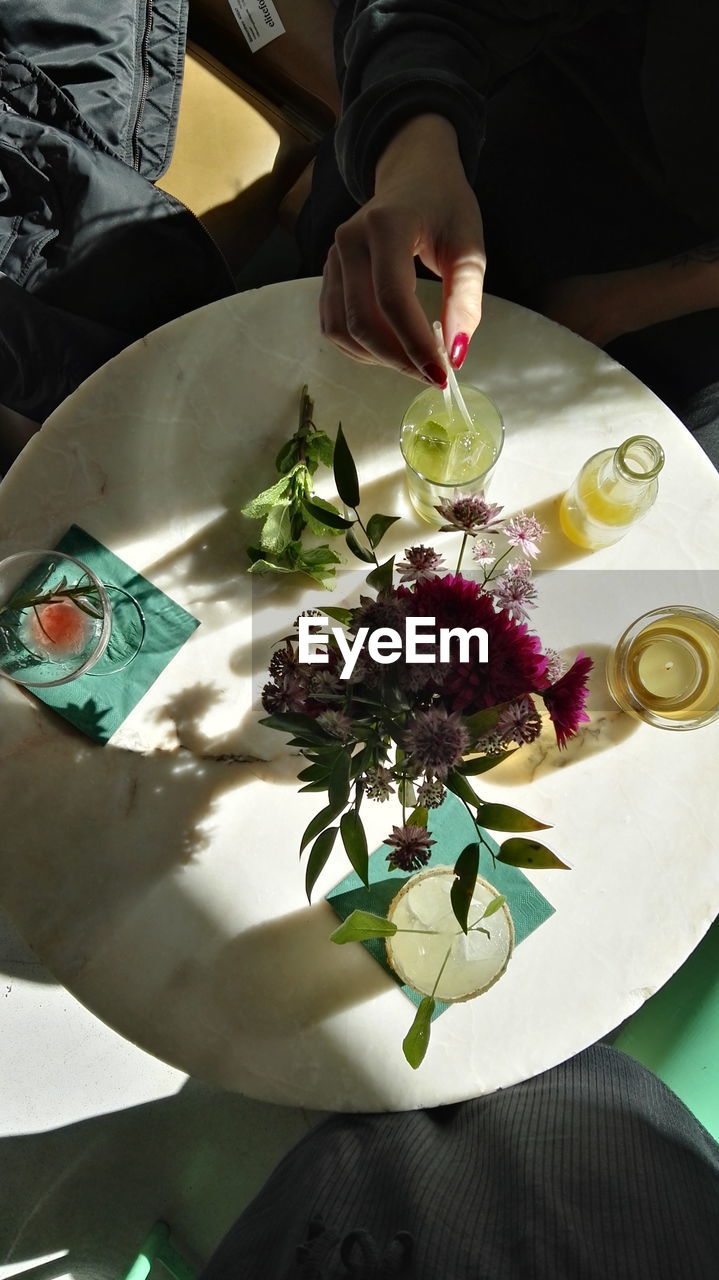 Cropped hand of woman having drink by vase on table