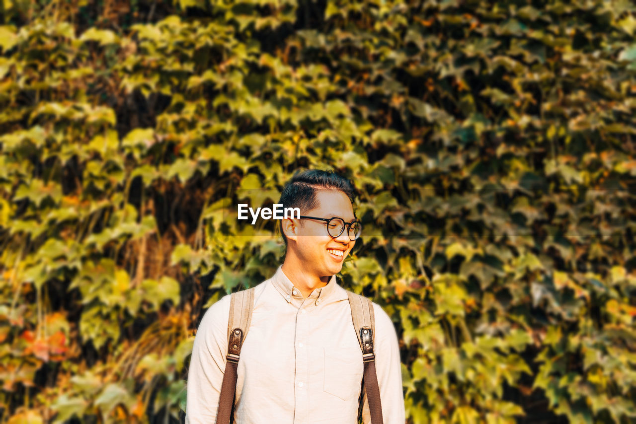 Smiling young man looking away against plants