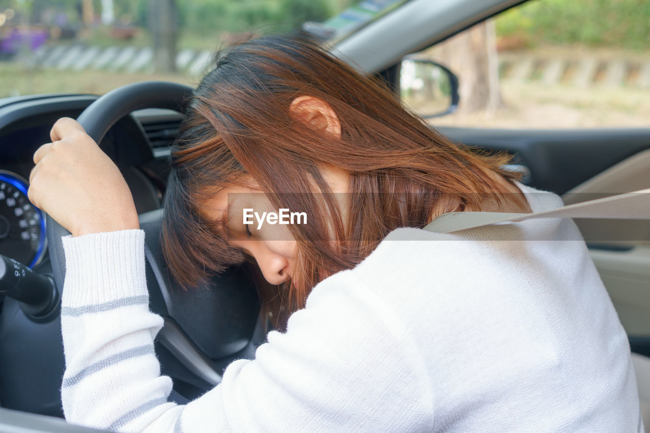 Woman with eyes closed on steering wheel in car