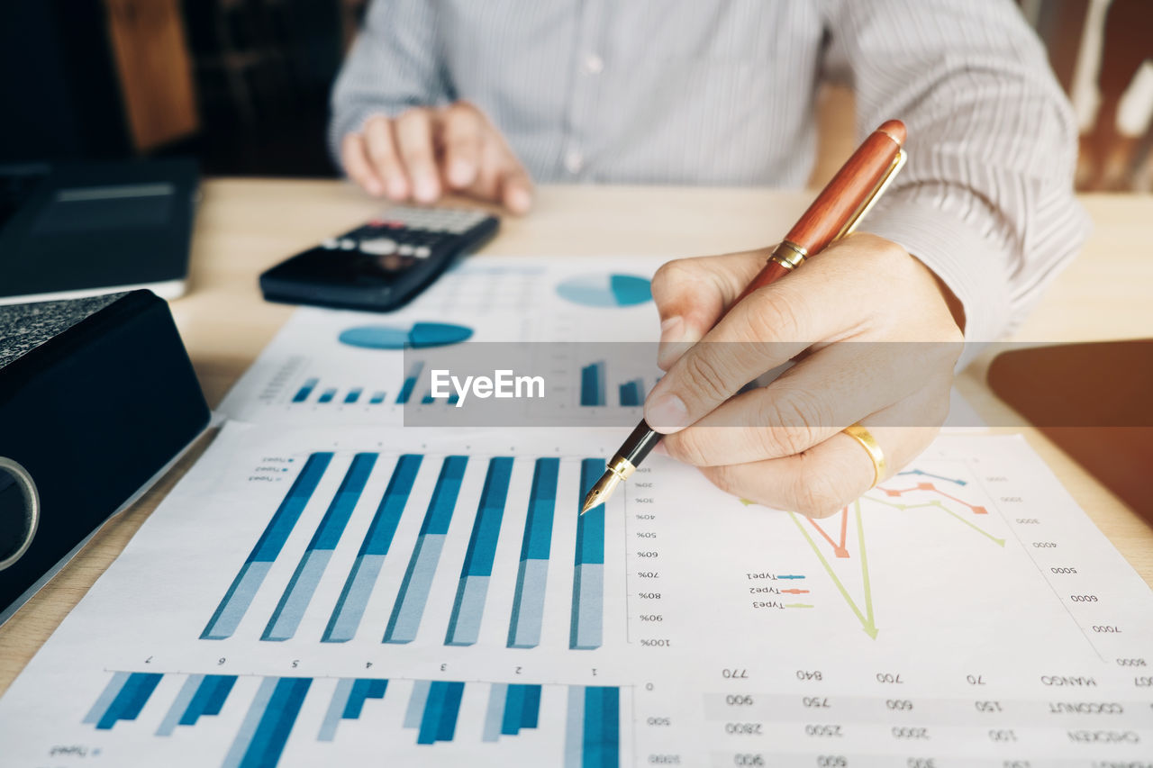 Midsection of businessman analyzing graphs at desk in office