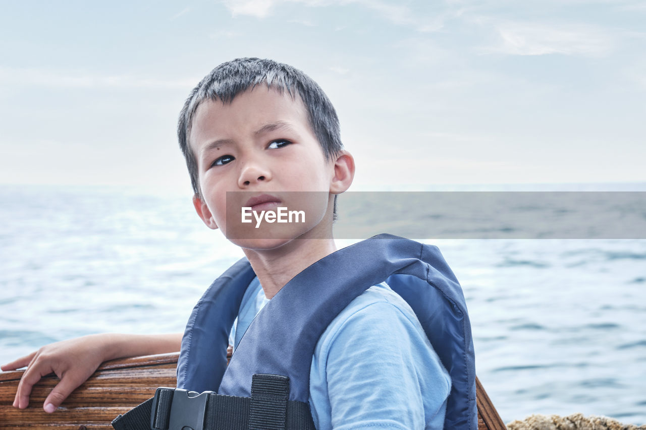 Portrait of boy looking away by sea against sky