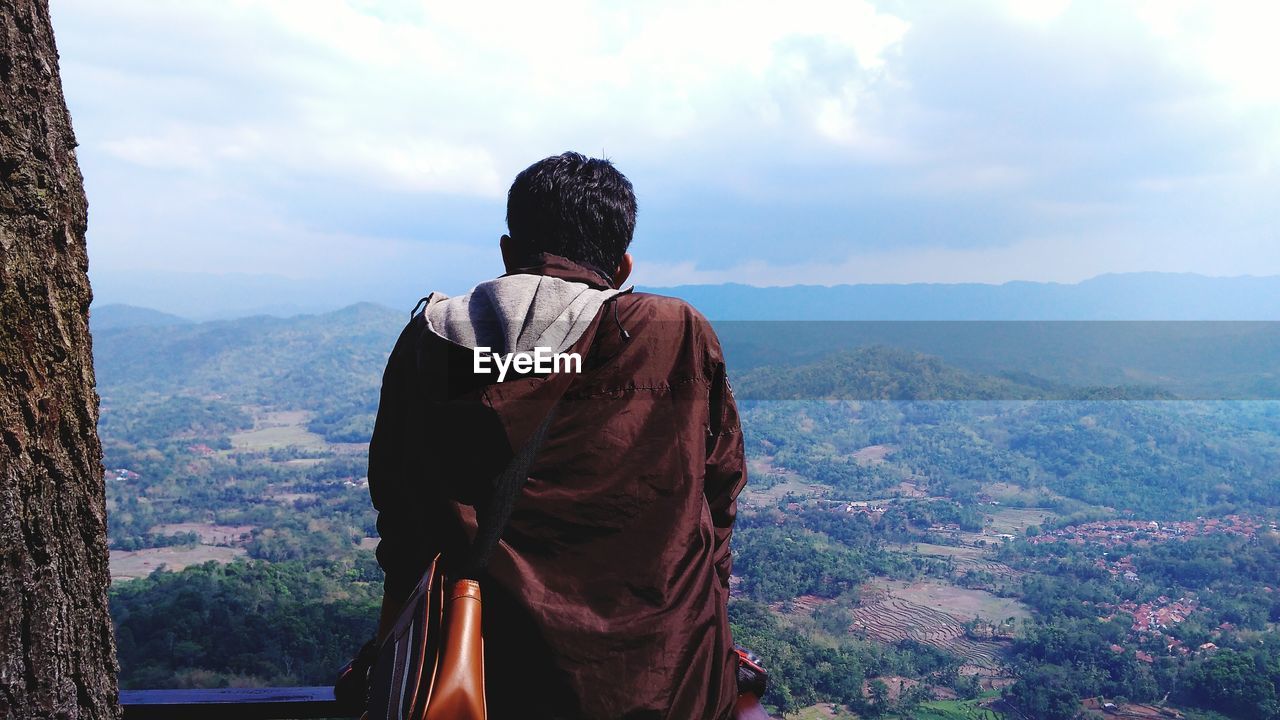 Rear view of man standing on mountain against sky