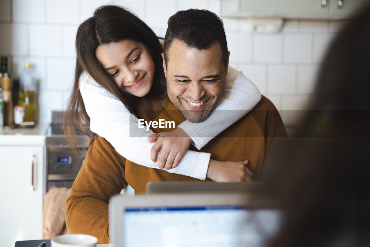 Smiling girl embracing father working on laptop at home