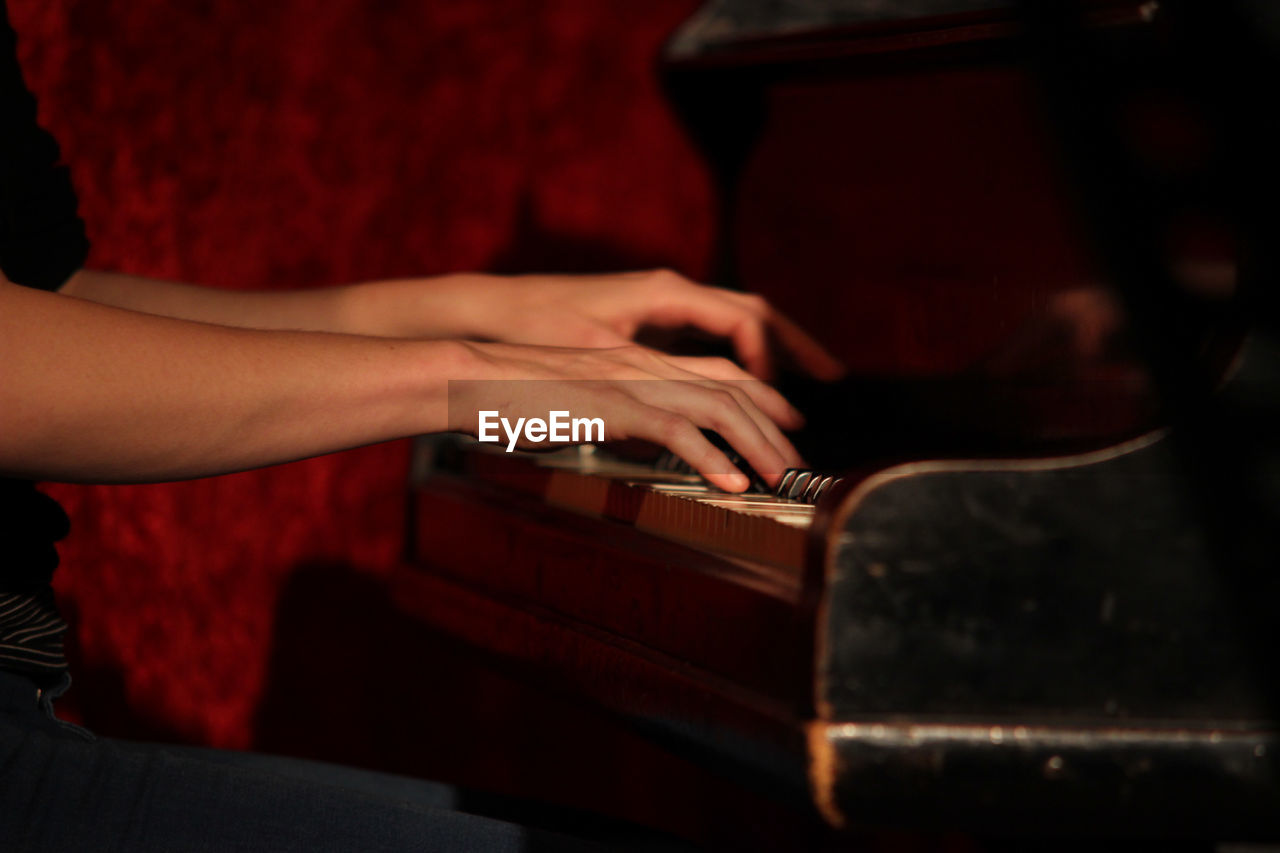 Midsection of man playing piano in darkroom