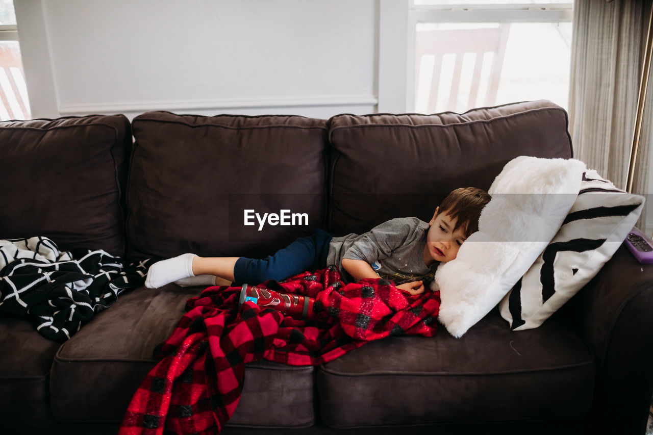 Young boy laying on couch in living room while sick with flu