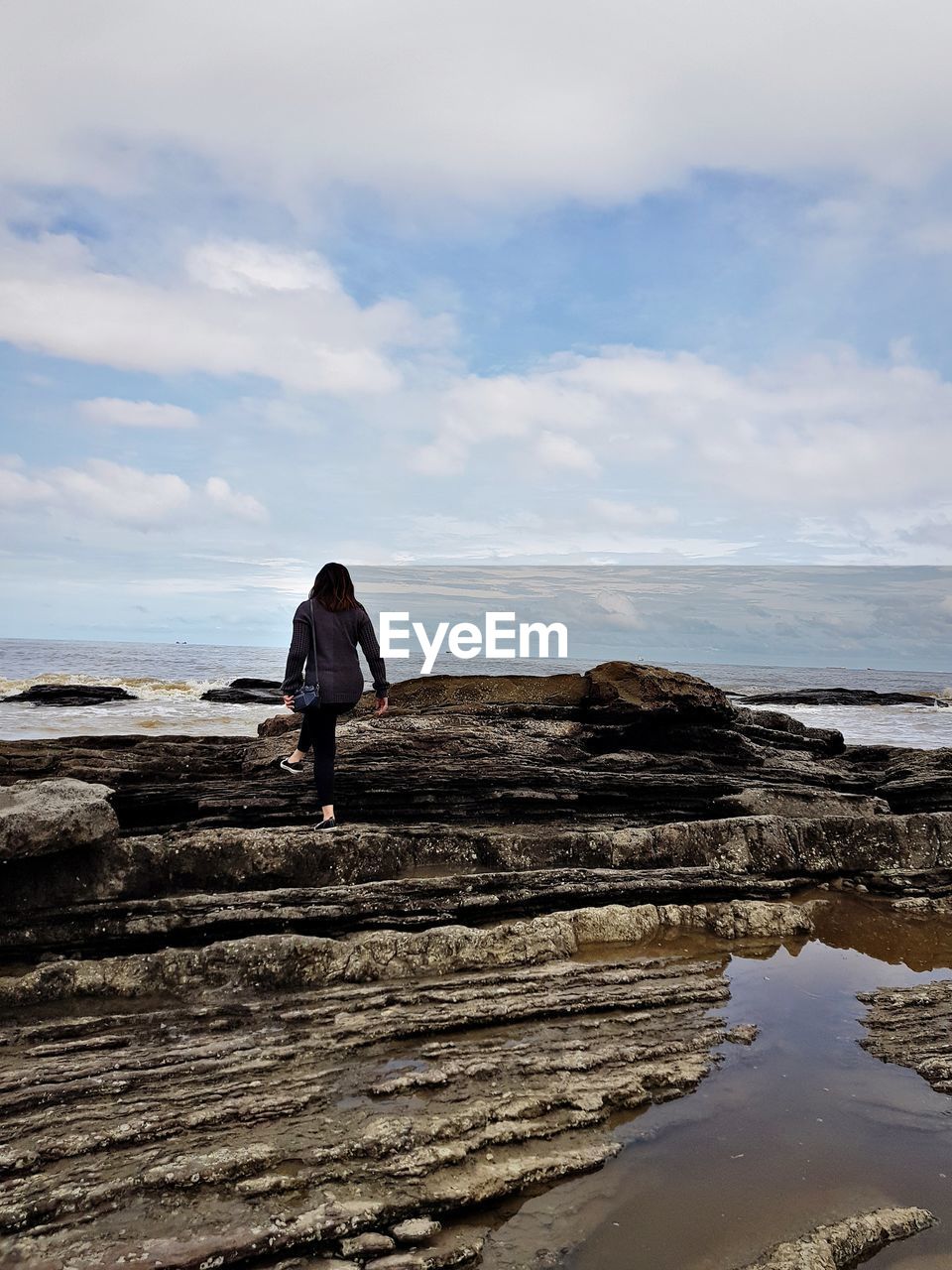 Rear view of woman standing on rocks at sea against sky