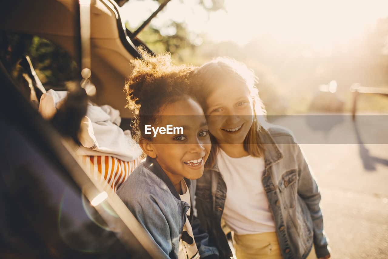 Portrait of smiling multi-ethnic girls in car trunk during picnic