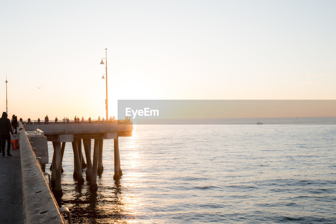 Scenic view of people standing on pier by sea against clear sky during sunset