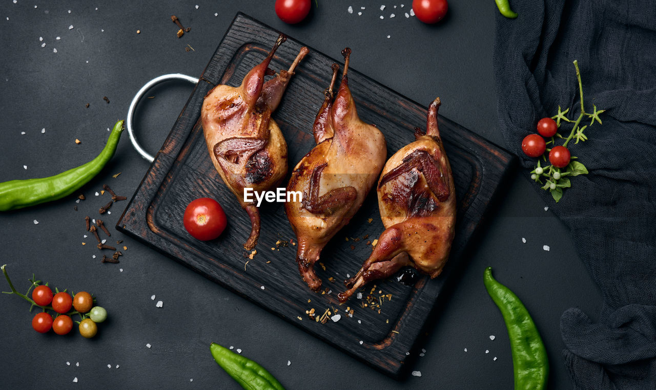 Frying carcasses of quails lie on a wooden board with vegetables, a black table