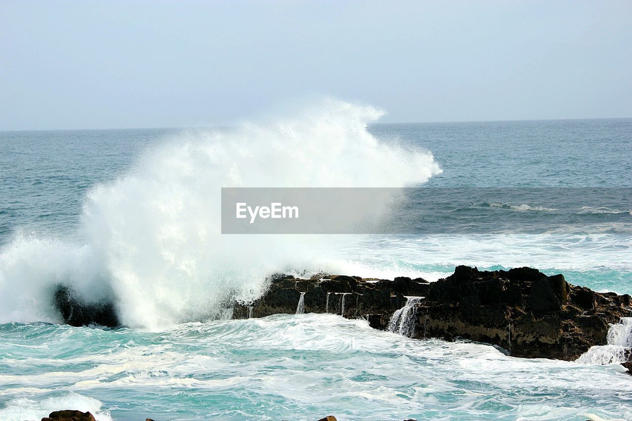 Waves splashing on sea against clear sky