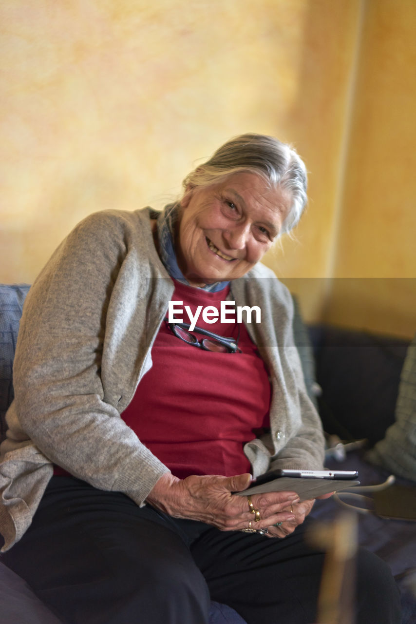 Portrait of smiling senior woman holding digital tablet at home