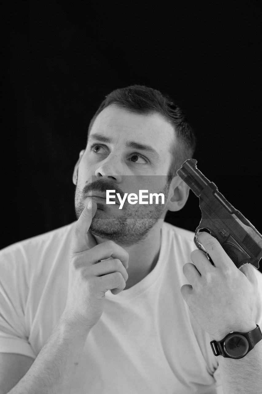 Thoughtful man attempting suicide with gun against black background