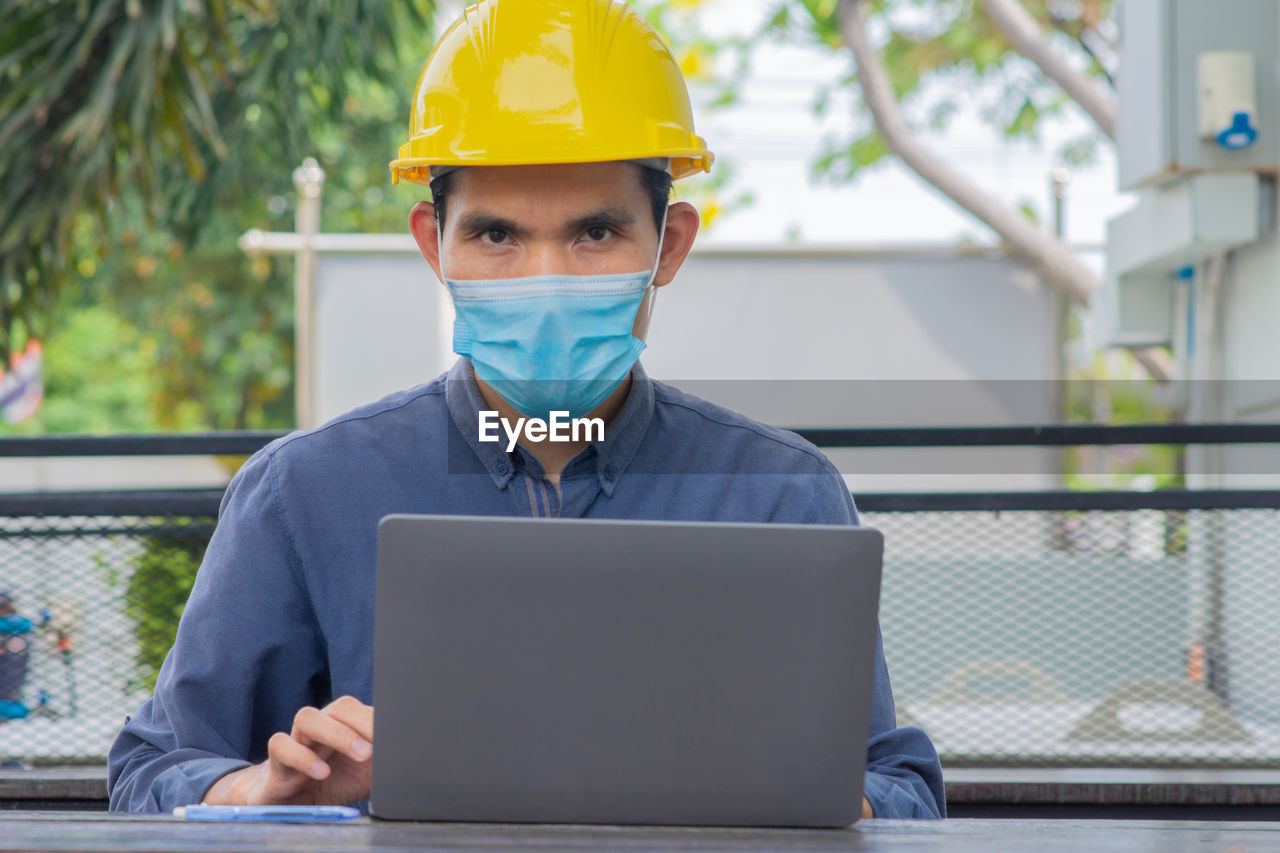 PORTRAIT OF MAN WORKING WITH MOBILE PHONE AT LAPTOP