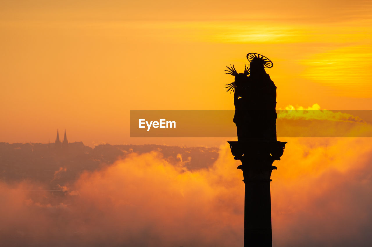 Silhouette statue on column against sky during sunset