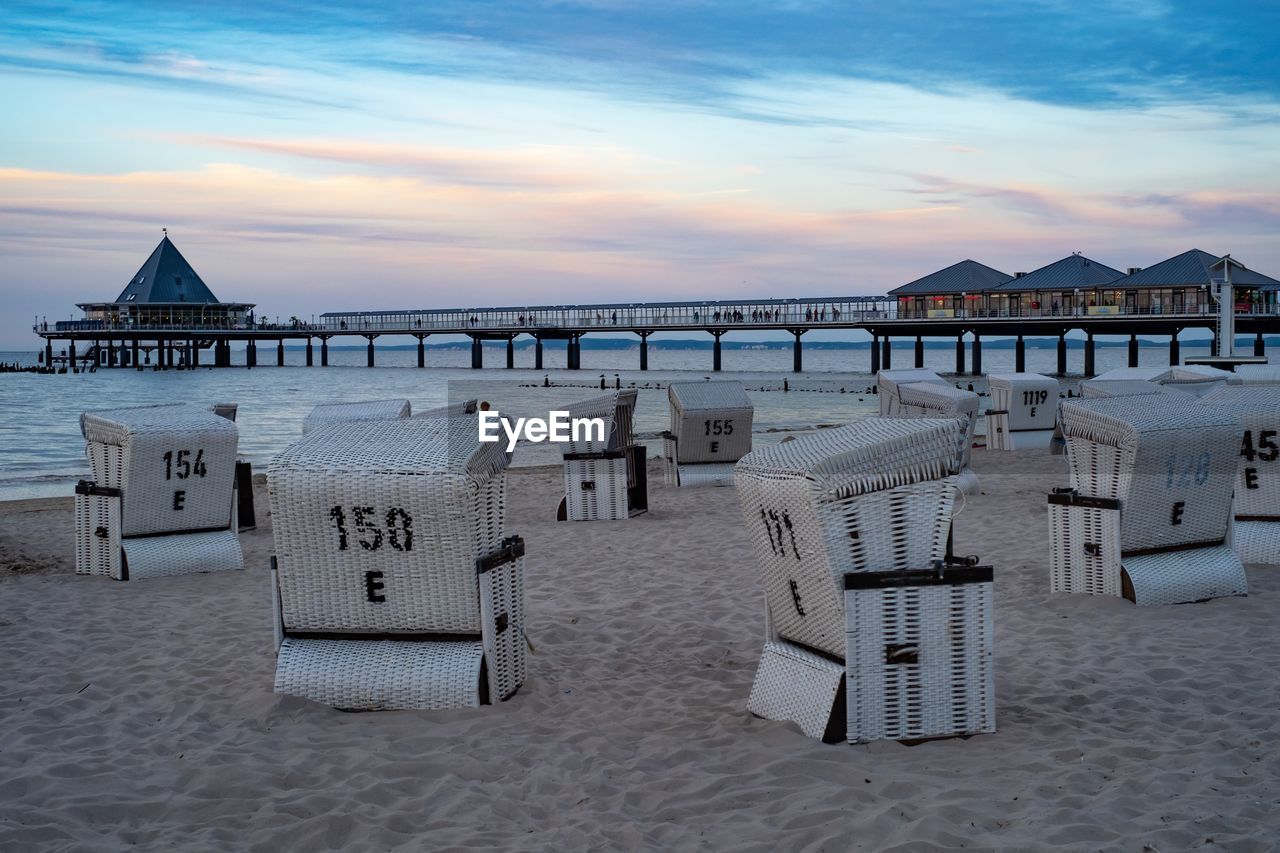 Hooded chairs on beach against sky during sunset