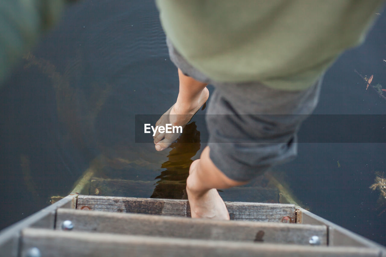 Low section of boy standing on wooden ladder over lake