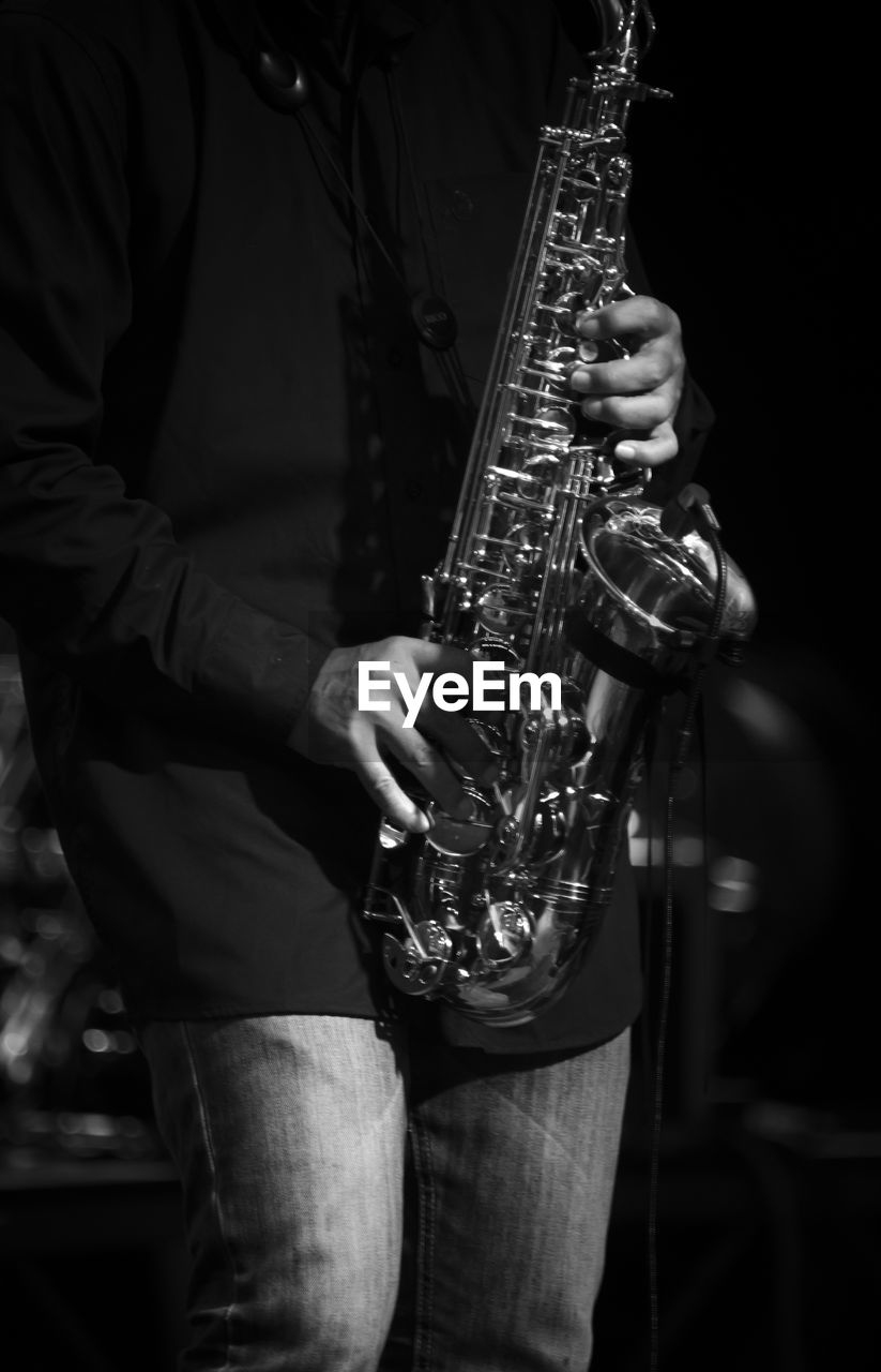 Midsection of man playing saxophone in darkroom